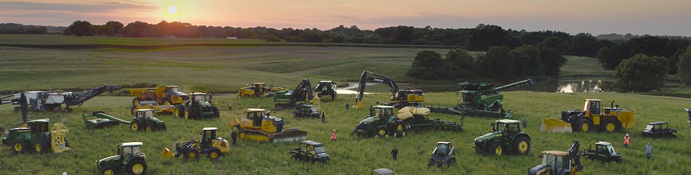 People walking amongst several types of John Deere equipment in a large field.