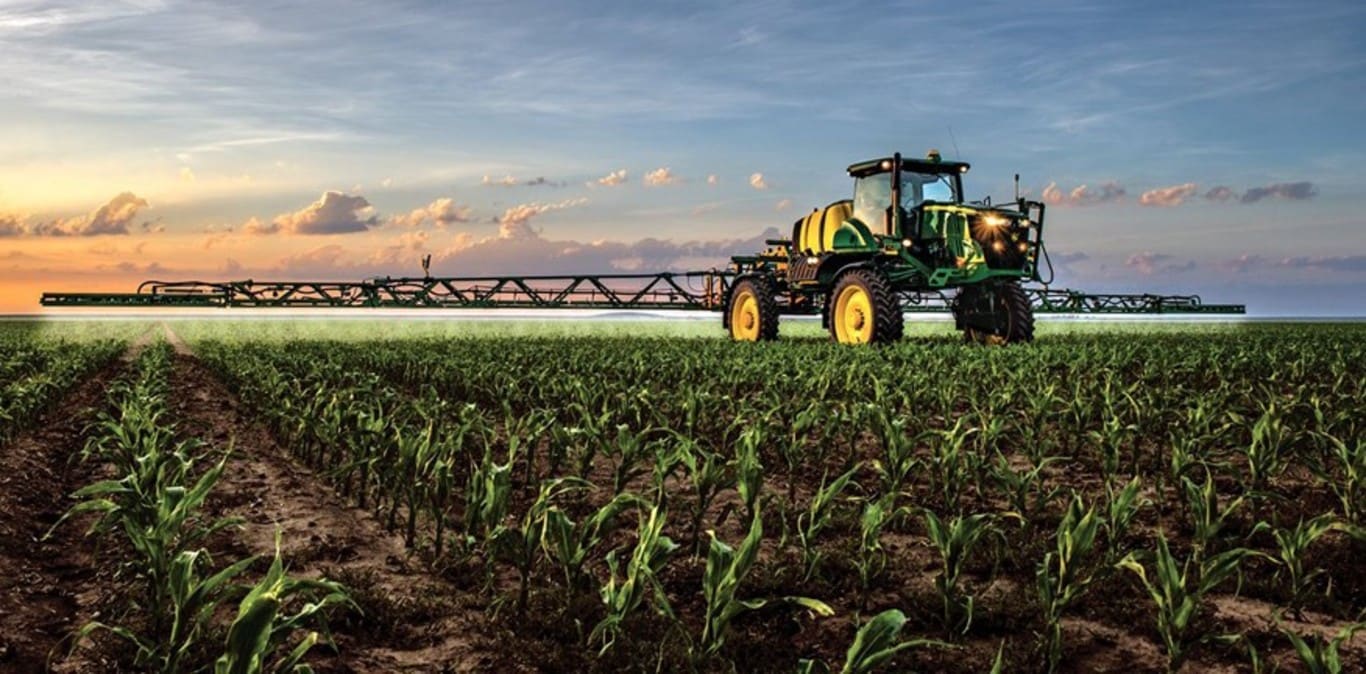 John Deere sprayer working in a corn field with the sunset in the background
